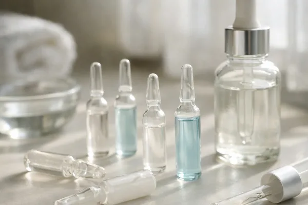 Mehrere Glasampullen mit klarer und blauer Flüssigkeit neben Serumflasche mit Pipette